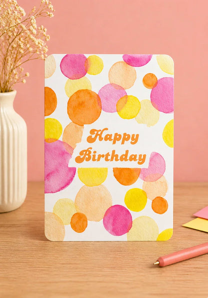 Carte d'anniversaire aquarelle aux pois colorés 'Happy Birthday' sur fond rose, idéale pour célébrer joyeusement.