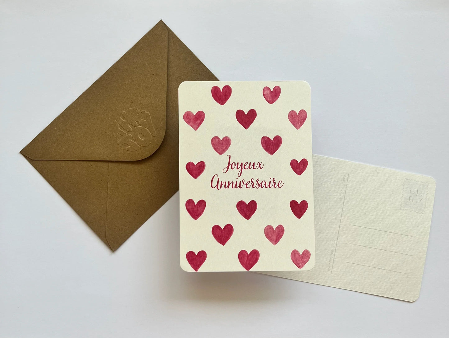 Carte d'anniversaire avec coeurs rouges et texte 'Joyeux Anniversaire', enveloppe kraft