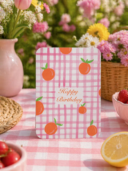 Carte d'anniversaire à motifs d'oranges sur fond à carreaux rose, idéale pour fêtes et célébrations en plein air