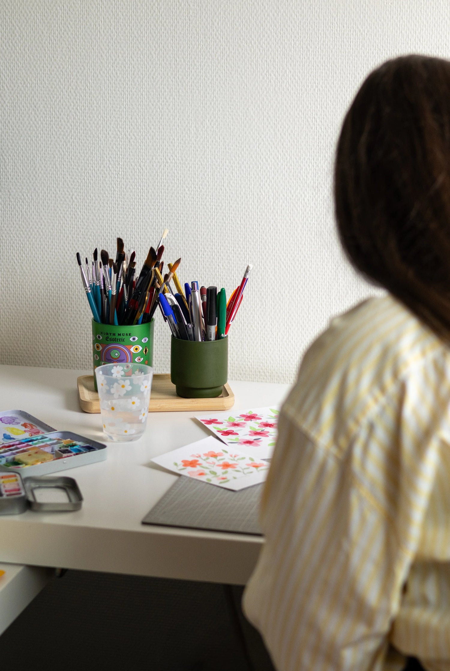 Artiste peignant des fleurs avec pinceaux et aquarelles sur bureau blanc